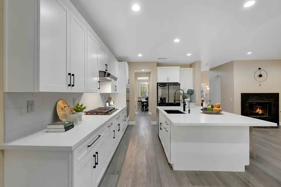 Kitchen remodeling by USA Home Remodeling: white shaker cabinets, quartz island with black faucet, wood-look flooring and a fireplace view in an Orange County home