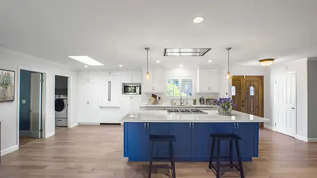 Open-concept kitchen remodel with royal blue island, white cabinets and wood-look flooring