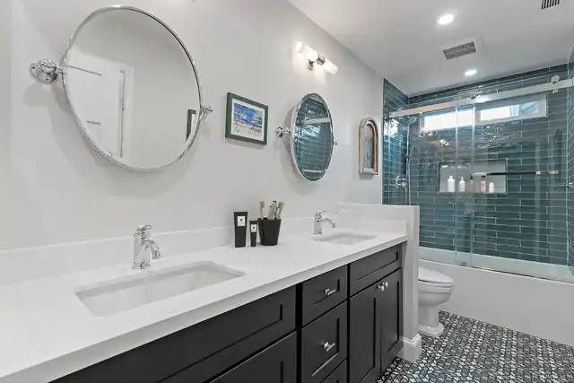 Anaheim guest bathroom remodel with a black double vanity, white quartz top, two round mirrors and a blue subway tile shower behind sliding glass