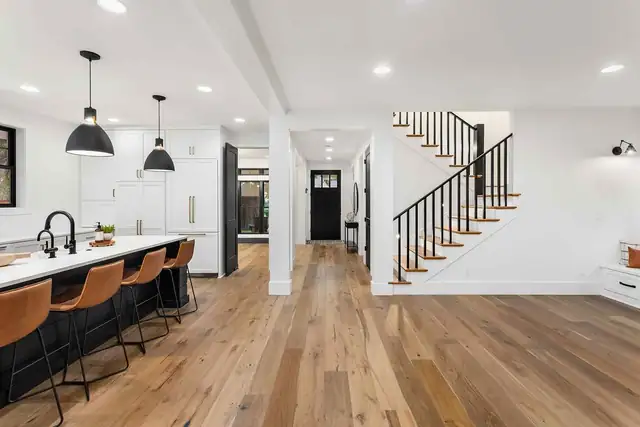 Complete home renovation with an open-concept kitchen, leather counter stools, wide-plank wood floors and a black stair railing
