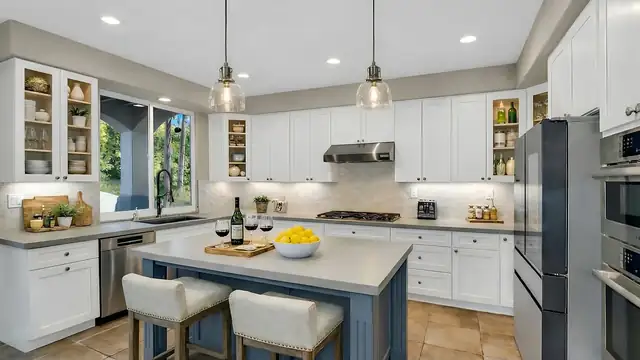 Kitchen remodel by USA Home Remodeling with white shaker cabinets, glass pendants over a blue island and stainless appliances