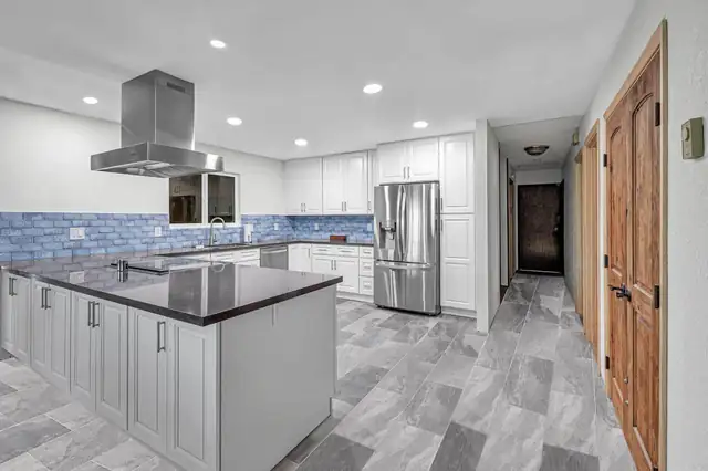 Orange County kitchen remodel with white cabinets, a dark quartz peninsula, stainless island hood, blue tile backsplash and gray plank tile floors
